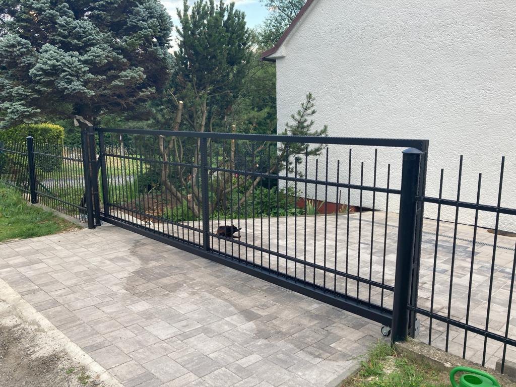 Černá samonosná posuvná brána s navazujícím svařovaným plotem na dlážděném vjezdu